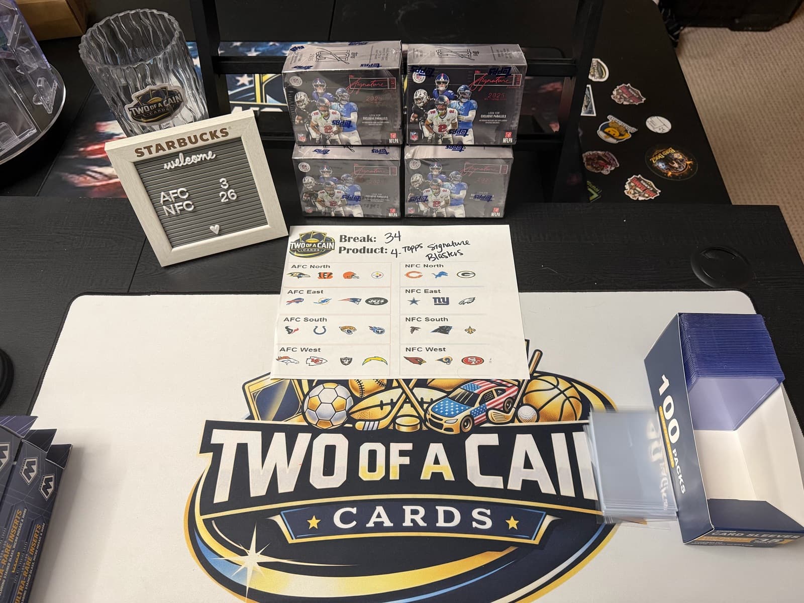 The Two of a Cain break table set up for a live break — sealed product stacked, team board printed, sleeves and toploaders ready